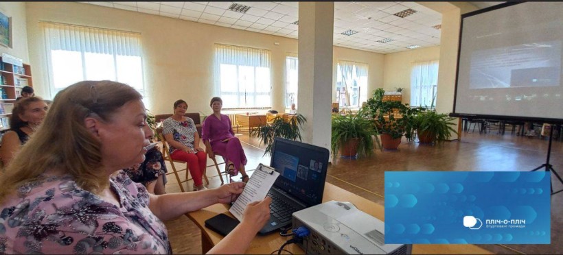 Читальний зал бібліотеки. Учасники марафону  сидять за столом, одна з них біля монітора ноутбука тримає лист з віршами.