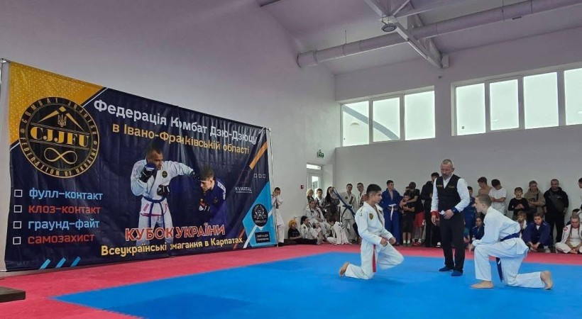 Спортсмени на спортивних матах, чекають початку змагань,поруч тренер.