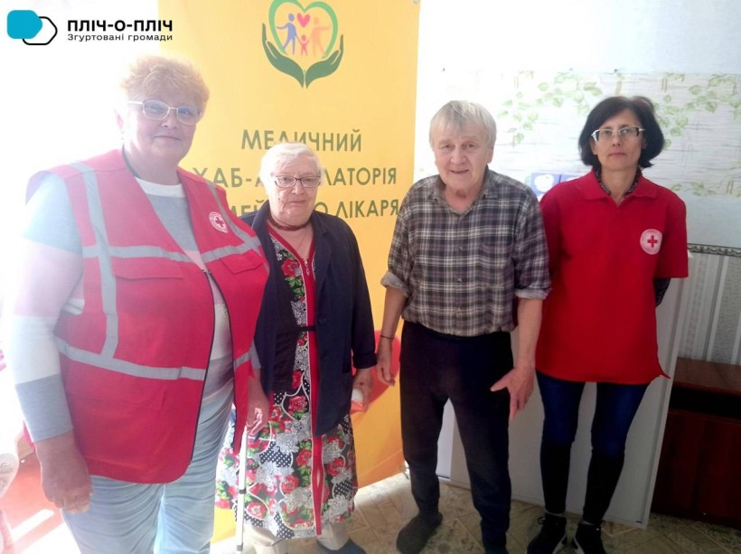 Спільне фото. Представниці Червоного хреста та чоловік з жінкою похилого віку.