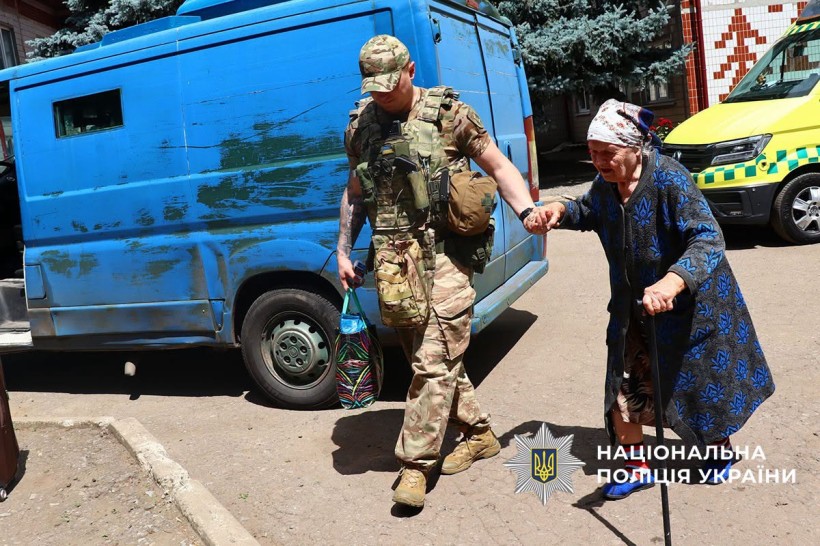 Поліцейський веде бабусю з палицею до евакомобіля
