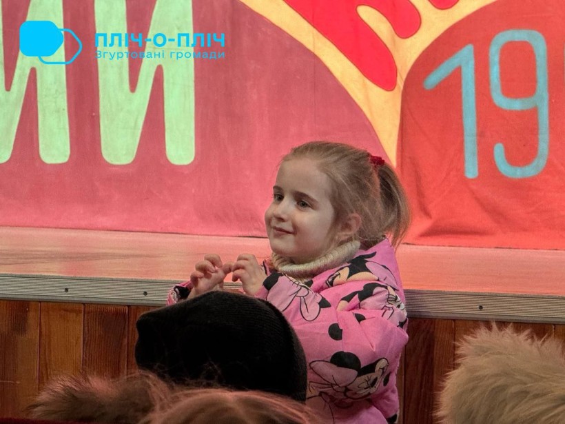 Маленька дівчинка у рожевому костюмі захоплено дивиться на сцену, намагаючись повторювати рухи.