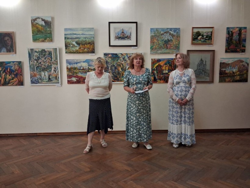Спікери виступають перед аудиторією на тлі стіни з картинами в художній галереї