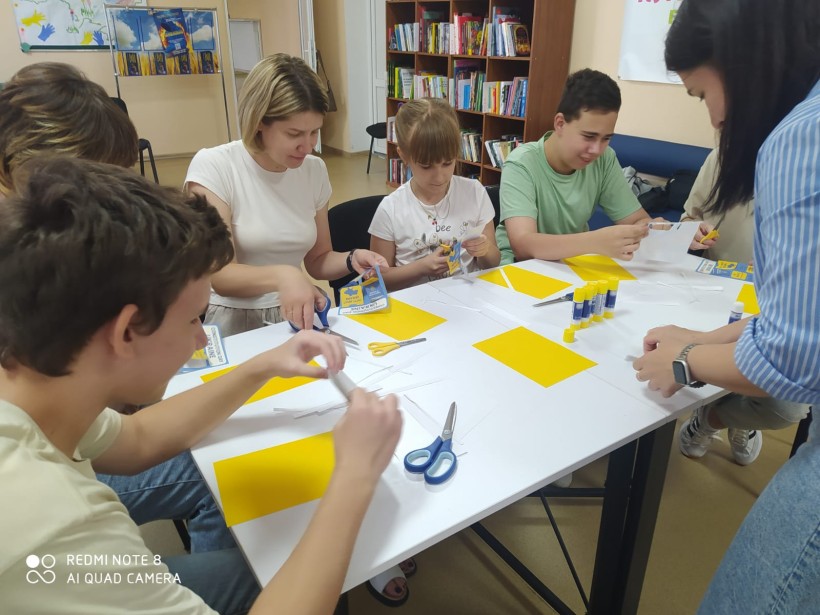 Діти й дорослі виготовляють лепбуки до Дня Конституції України: працюють із ножицями, клеєм і жовто-блакитними матеріалами.
