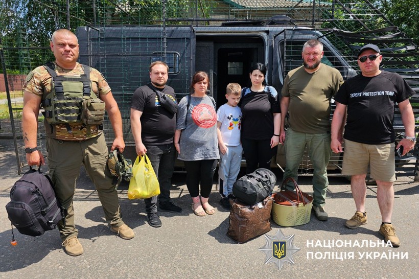 Вагітна жінка та її чоловік разом, дитина та матір разом з поліцейськими біля броньованого автомобіля біля пункту евакуації.