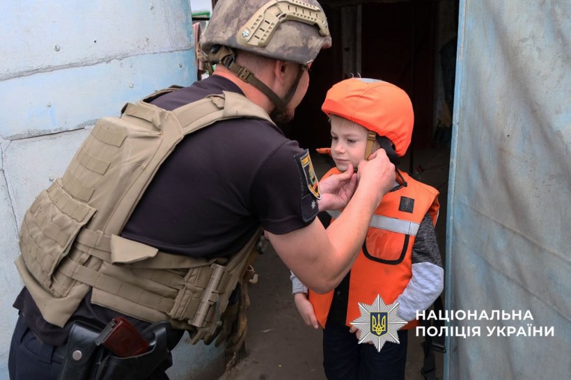 Поліцейський допомагає дитині вдягнути бронежилет та каску