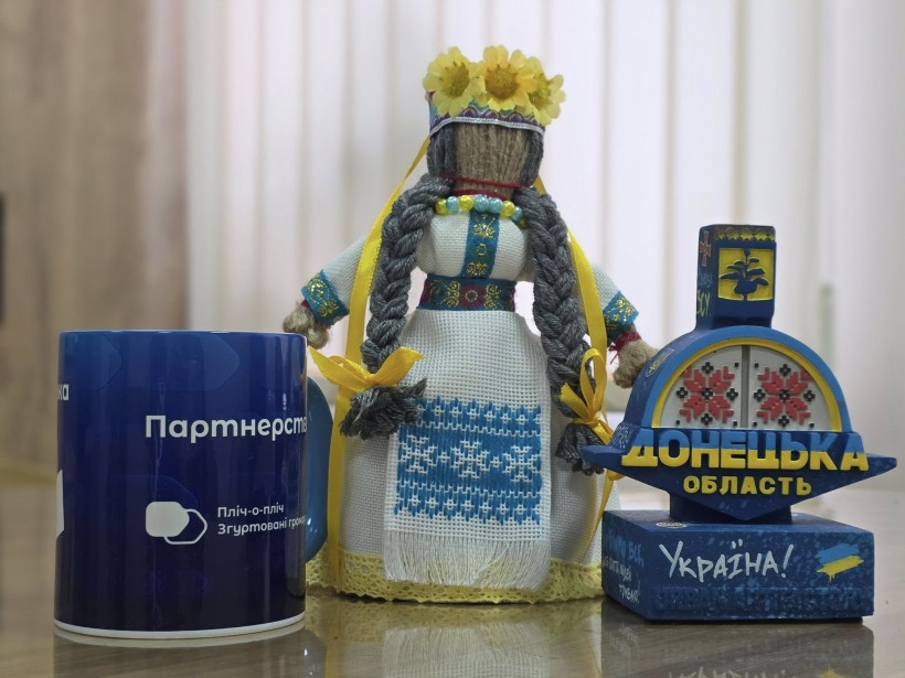 Сувенірна продукція. Стела Донеччини, лялька мотанка та синя кружка з написом про партнерство
