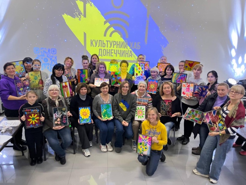 Дорослі відвідувачі хабу на груповому фото з картнами в рамках, які намальовані на арттерапії