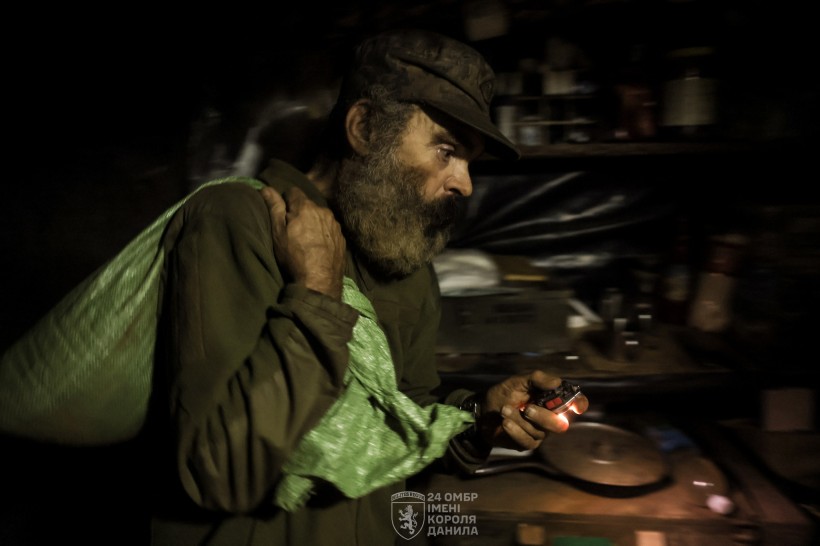 Військовий тримає зелений мішок на плечах у руках ліхтарик.