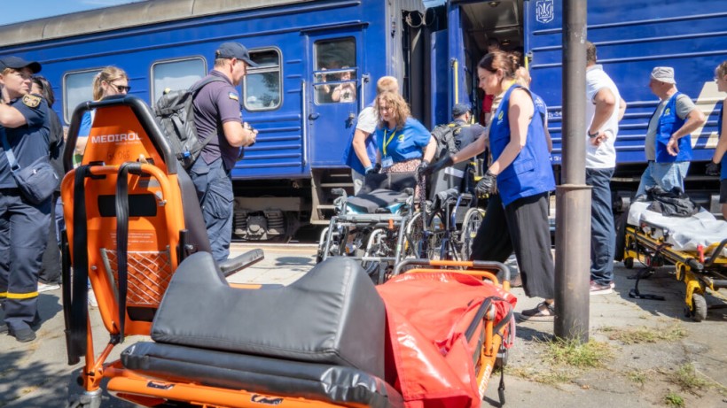 Людей у кріслах колісних вигружають з евакуаційного потяга волонтери та представники ДСНС