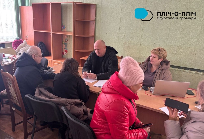 Начальник Лиманської мііської військової адміністрації Олександр Журавльовсидить за столом на зустрічі з мешканцями громади.