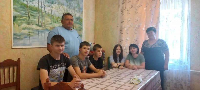 Великий стіл за столом сидять хлопці, дівчата та жінка. Чоловік стоїть біля стіни