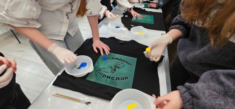 На столі лежить футболка з надписом міст Селидове та Борислав , діти розмальовують літери жовто -блакитними фарбами