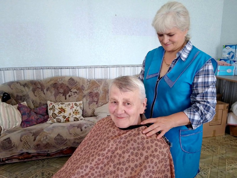 Літня жінка з підстриженим волоссям, посміхається, поруч стоїть перукар, яка тримає її за плечі.