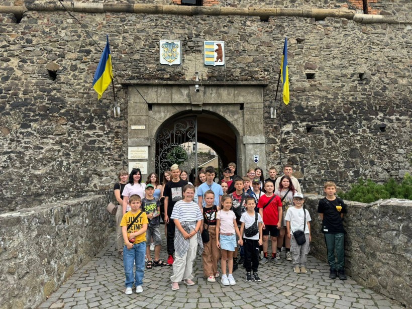 Спільне фото дітей. Діти стоять біля входу до замку, зверху прапори України.