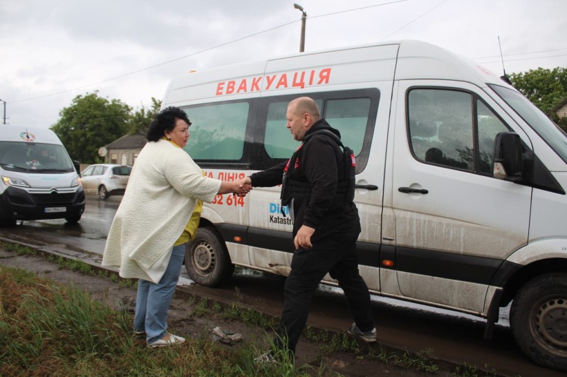 Жінка та чоловік вітаються на фоні евакуаційного автомобіля
