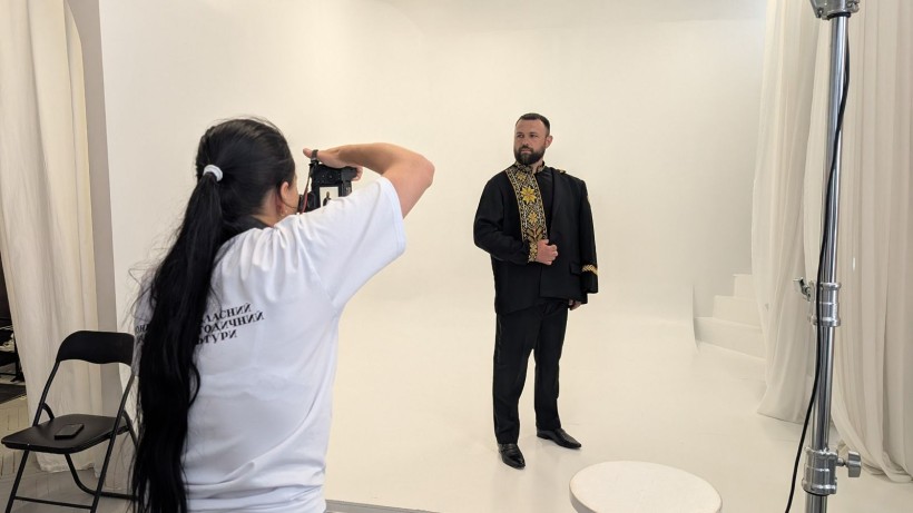 Фотографиня знімає чоловіка у чорному костюмі з вишитими золотими елементами