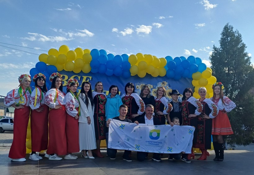 Спільне фото учасників заходу. Жінки у національному вбранні. Позаду жовто-блакитні кульки. Попереду прапор громади.