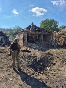 Зруйнований ворожим обстрілом будинок поруч з яким стоїть правоохоронець