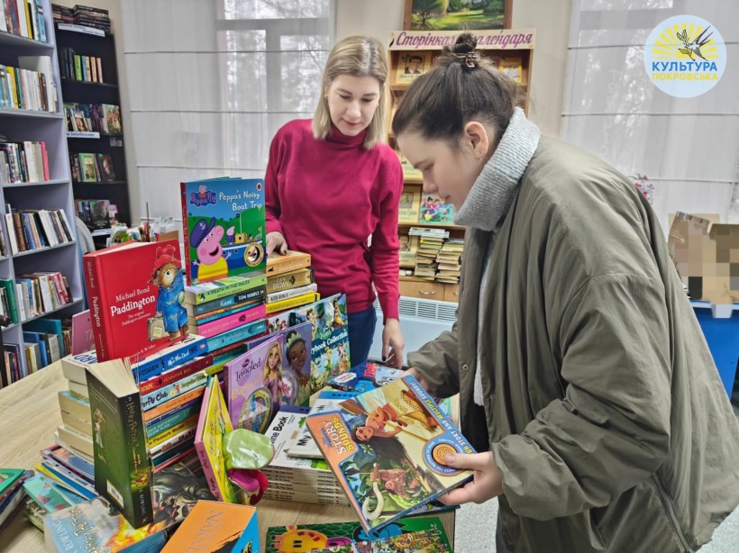 Бібліотекарка Покровської бібліотеки показує відвідувачці нові надходження англомовних книжок