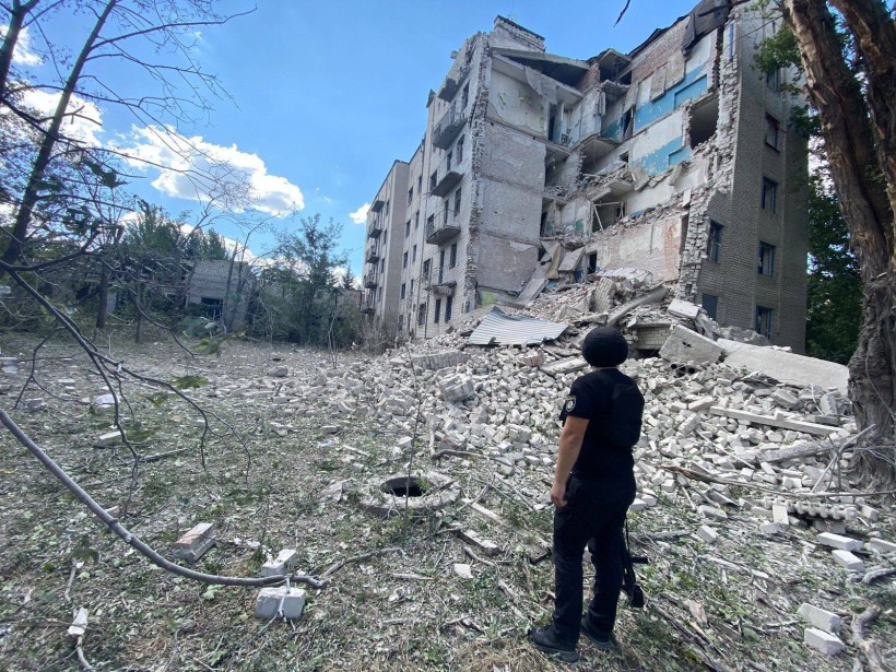 Правоохоронець стоїть біля зруйнованої окупантами багатоповерхівки.