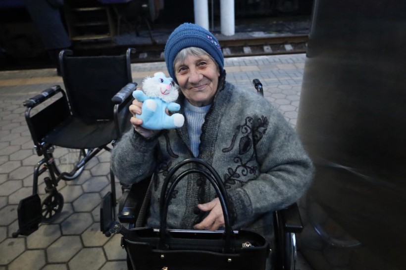 Евакуація літньої жінки, поруч стоїть крісло колісне, жінка тримає дитячу іграшку та посміхається