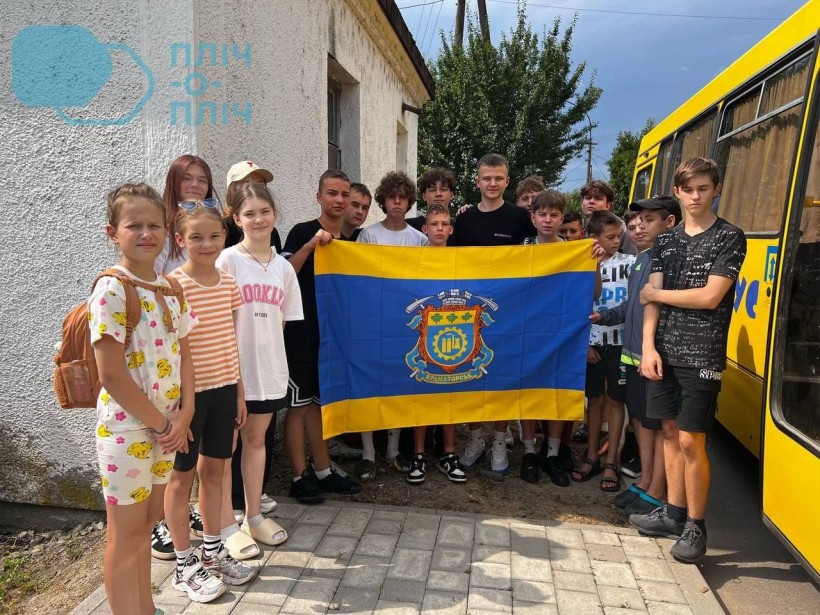 Група дітей стоїть біля шкільного автобуса та тримає прапор Краматорська
