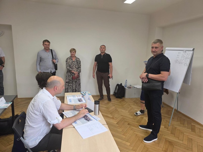 Учасники делегації спілкуються з жінкою та чоловіком які сидять за столом.