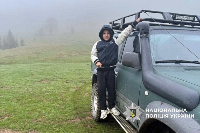 Хлопчик стоїть біля машини, позаду гори