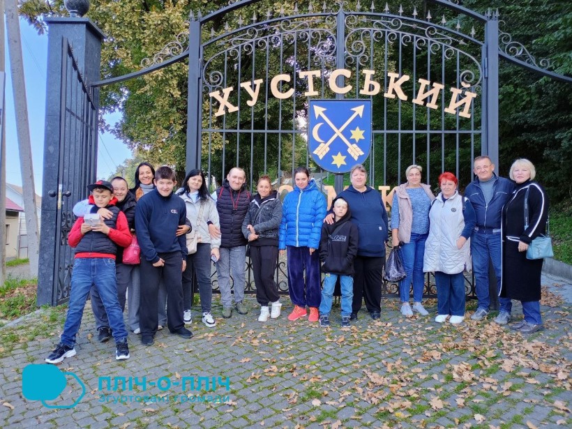 Спільне фото. Переселенці біля воріт краєзнавчого музею. На задньому плані герб міста та надпис Хустський.