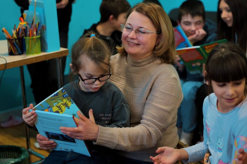 Начальницяуправління культури і туризму Вікторія Точена тримає на руках дитину з книжкою, навкруги інші діти читають подаровані книжки