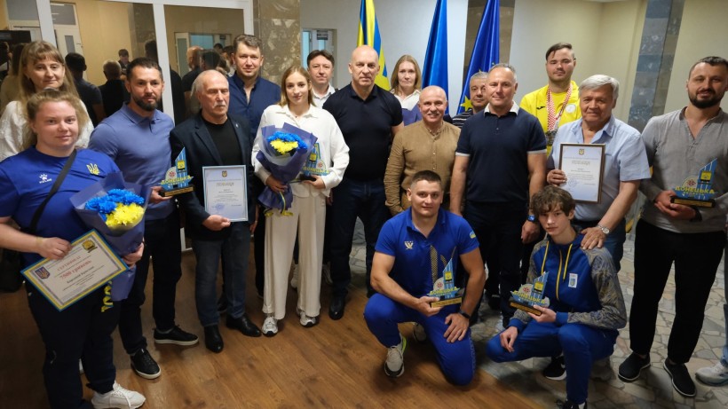 Вадим Філашкін зі спортсменами та тренерами, які тримають грамоти, квіти та пам'ятні подарунки