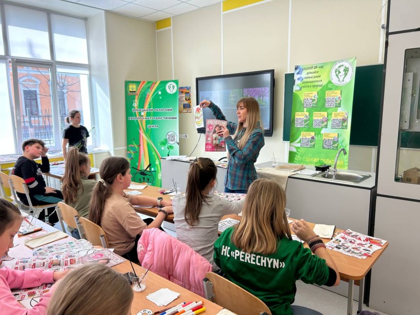 Керівниця гуртка екологів пояснює дітям як виготовити екоколаж
