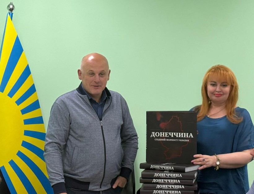 Перший заступник голови Юрій Винокуров та в.о. голови Краматорської райдержадміністрації, начальника районної військової адміністрації Вікторія Набокова, стоїть біля прапора Донеччини. Вікторія тримає книгу про історію війни на Донеччині.