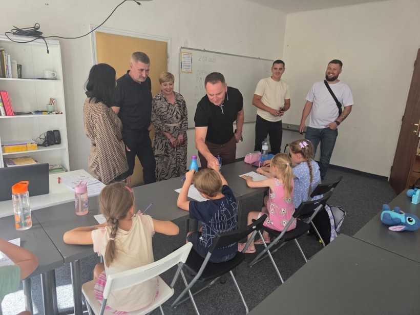 Наталія Чукова та представники делегації спілкуються з дітьми, які малюють, та тиснуть руку хлопцю.