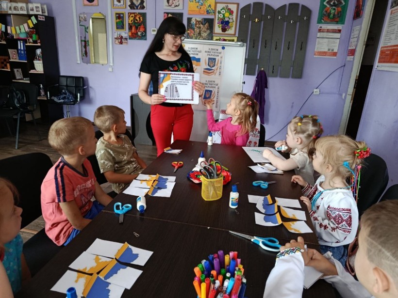 Діти сидять за столом, фахівець Центру розповідає про державні символи та орнаменти, демонструючи зображення