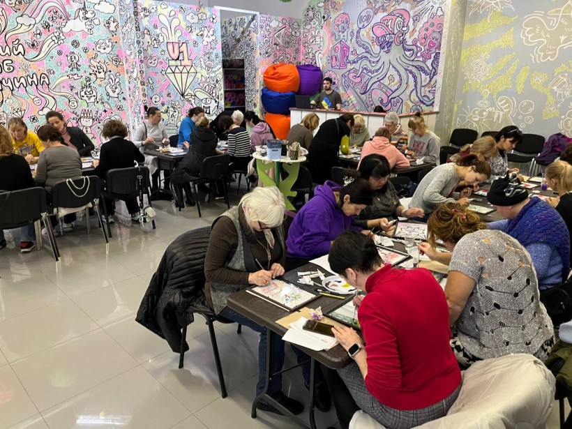 Учасники арттерапії за столами малюють картини