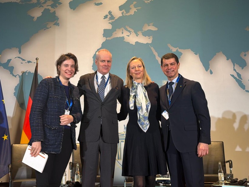 Групове фото чотирьох спікерів конференції НАТО, які стоять поруч і посміхаються на фоні карти світу та логотипу заходу.