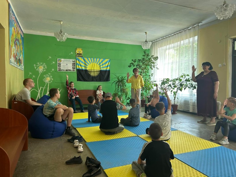Діти сидять та підіймають руку вгору, беруть участь у грі