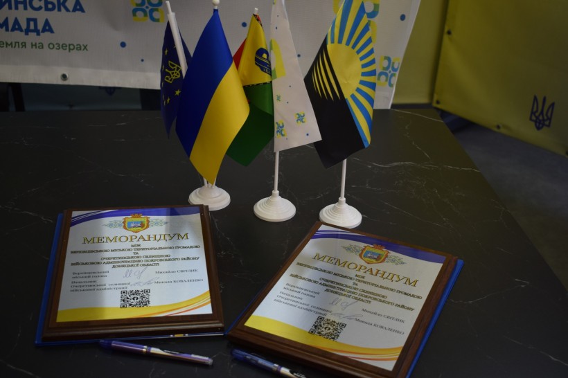 На столі лежать підписані Меморандуми про співпрацю між Верхівцівською міською і Очеретинською селищною територіальними громадами та стоять прапори: громад, України та Донеччини.