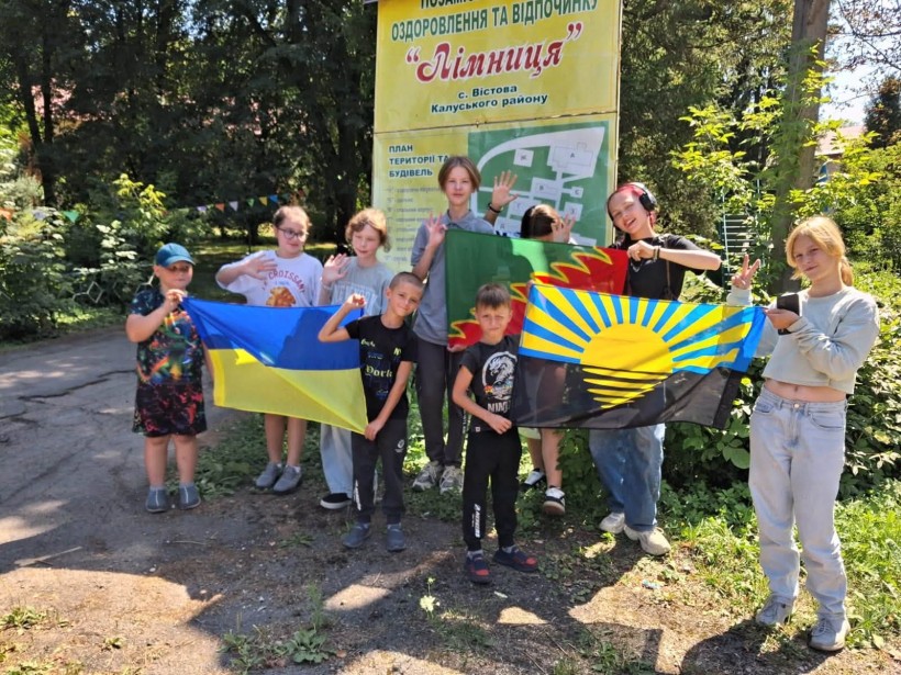 Діти тримають прапори України, Донеччини та Авдіївської громади на фоні банеру "Лімниця"