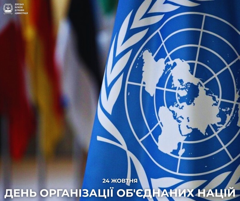 Зблизька синій прапор ООН з емблемою у вигляді карти світу на тлі розмитих різнокольорових прапорів. Напис «День Організації Об'єднаних Націй».