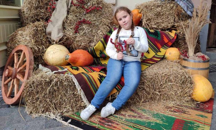 Дівчина на фоні осінньої композиції із сіна, гарбузів та калини.