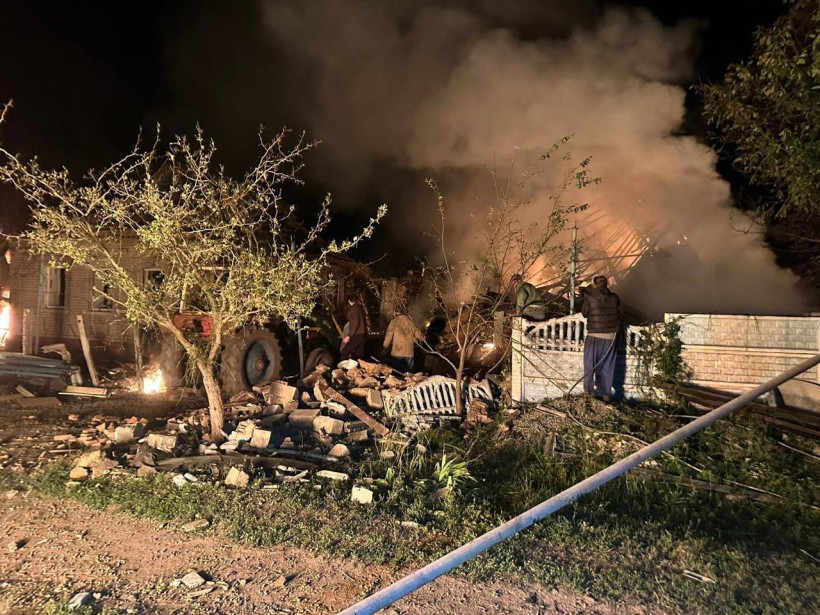 Зруйнований приватний будинок та паркан після ворожого обстрілу, де пожежники гасять вогонь.