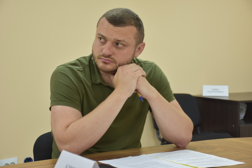 Представник адміністрації сидить за столом та слухає доповідь.