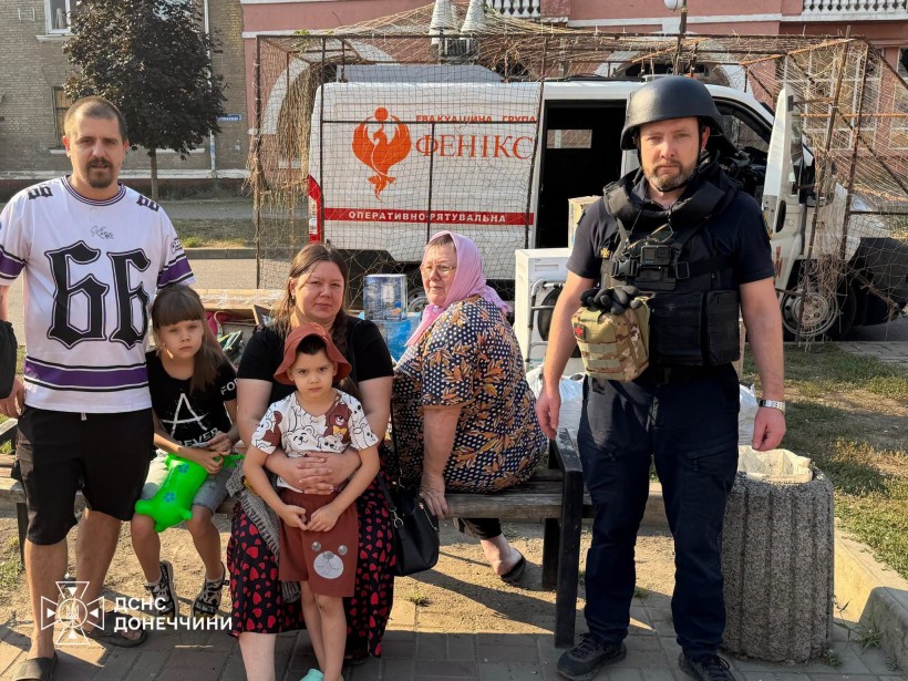 Родина з дітьми сидить на лавці, поруч - рятувальник групи "Фенікс"