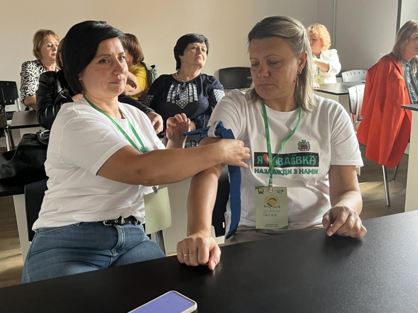 Учасниці тренінгу вчаться надавати першу домедичну допомогу, тренуючись накладати на передпліччя джгут.