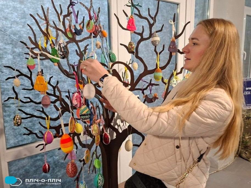Жінка вішає писанки на дерево.