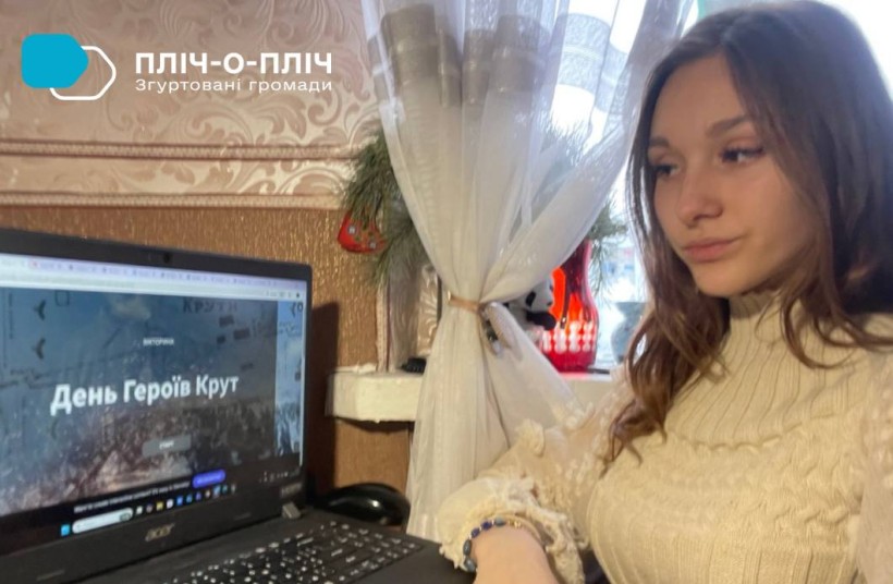 Учениця Бахмутського центру професійно-технічної освіти, сидить біля екрану монітора,на екрані слайд про Героїв Крут.