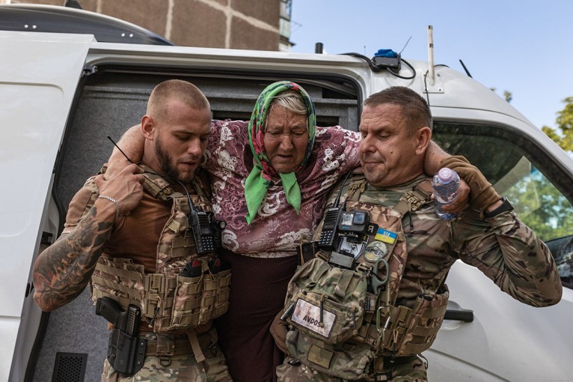 Жінка похилого віку яку несуть поліцейські до броньованого автомобіля.