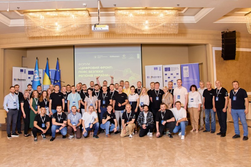 Спільне фото учасників форму в середні приміщення. На задньому плані лед-єкран та прапори: ООН, України та Євросоюзу.